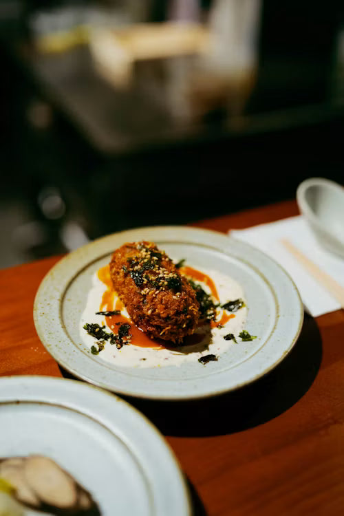Croqueta dorada sobre un plato de cerámica con salsa y hierbas